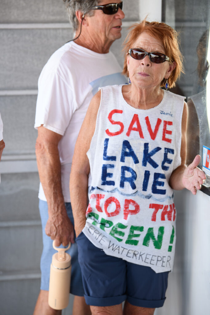 A woman leans against the Jet Express boat wall wearing a shirt that says, Save Lake Erie | Stop the Green.