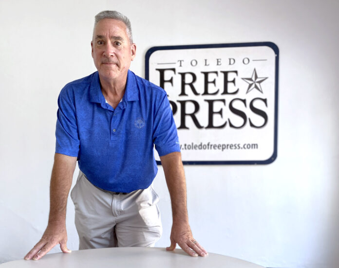 Tom Pounds leans on a table with a Toledo Free Press sign behind him.