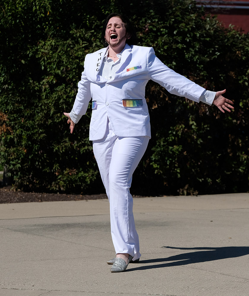 Trans man lip-syncing and wearing a white suit.