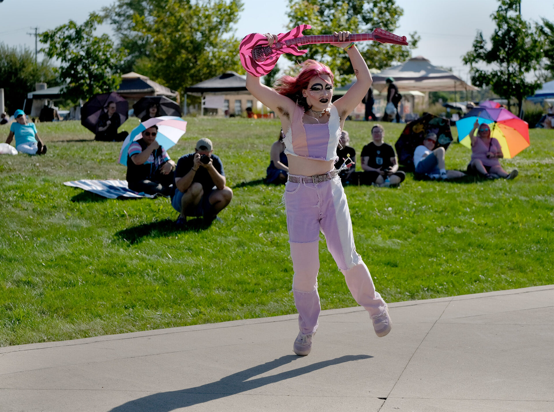 Trans man performaning on stage with pink guitar raised above her head.